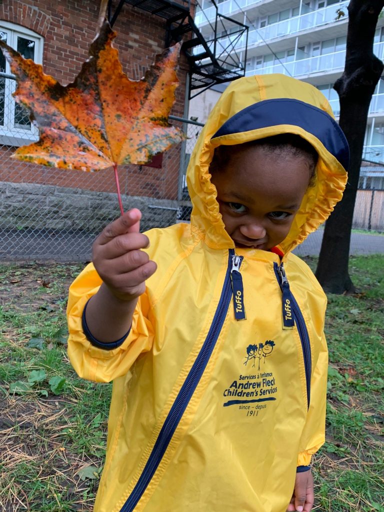 Black child in yellow raincoat holding a red leaf.
