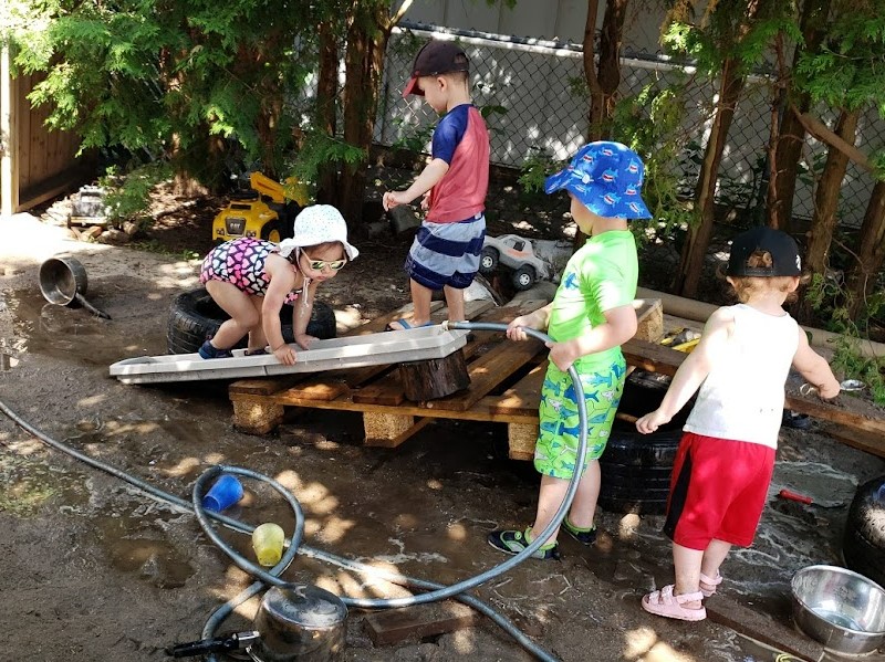 Children playing with water hose on wooden structure.