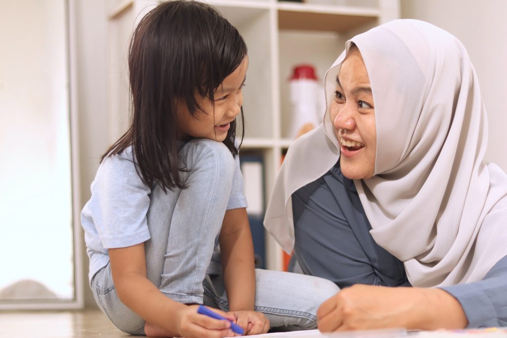 Hijabi educator coloring with child.
