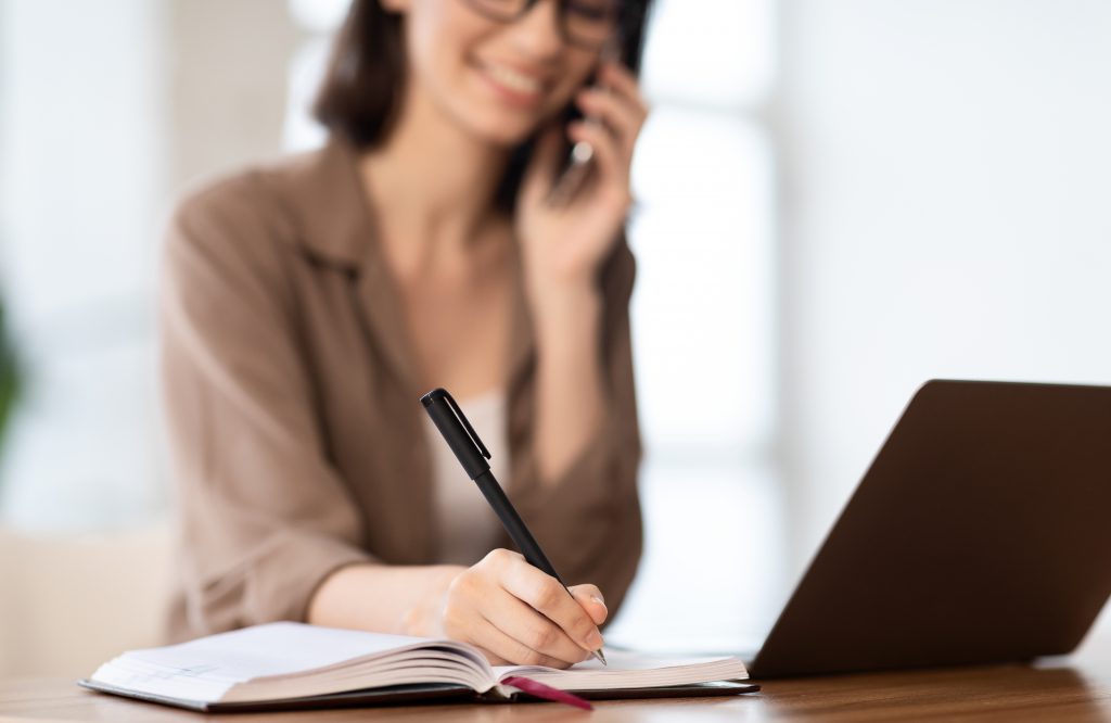 Woman talking on the phone and writing in agenda.