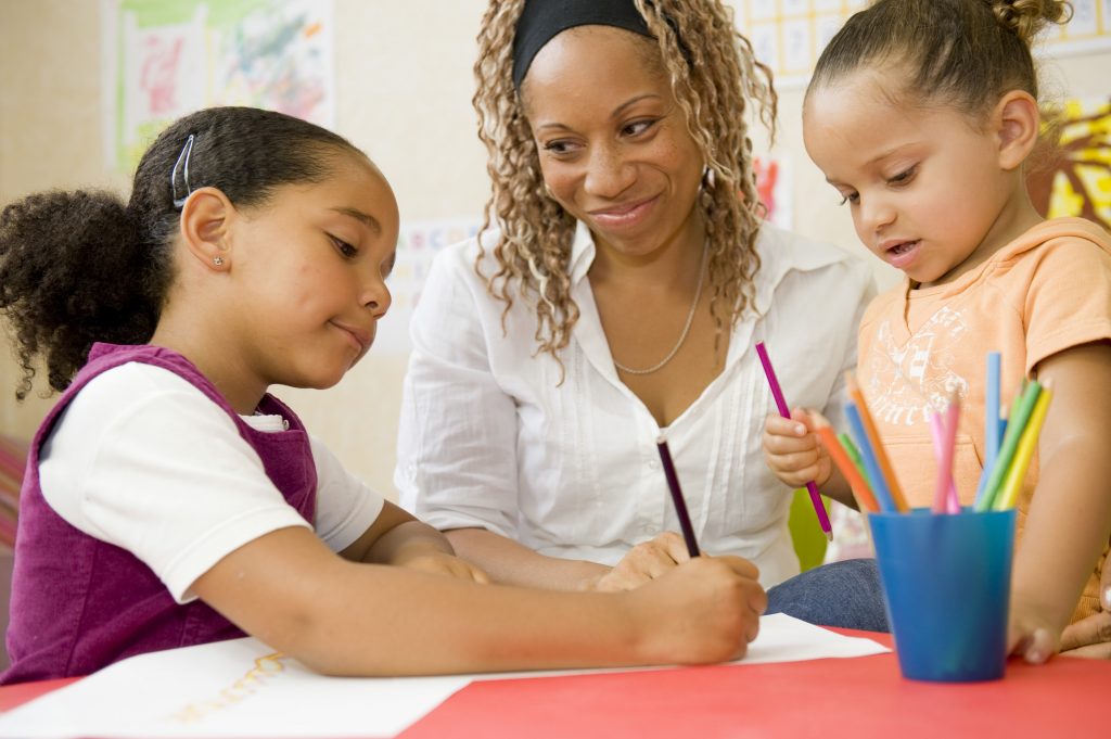 Educatrice qui colorie avec des enfants.