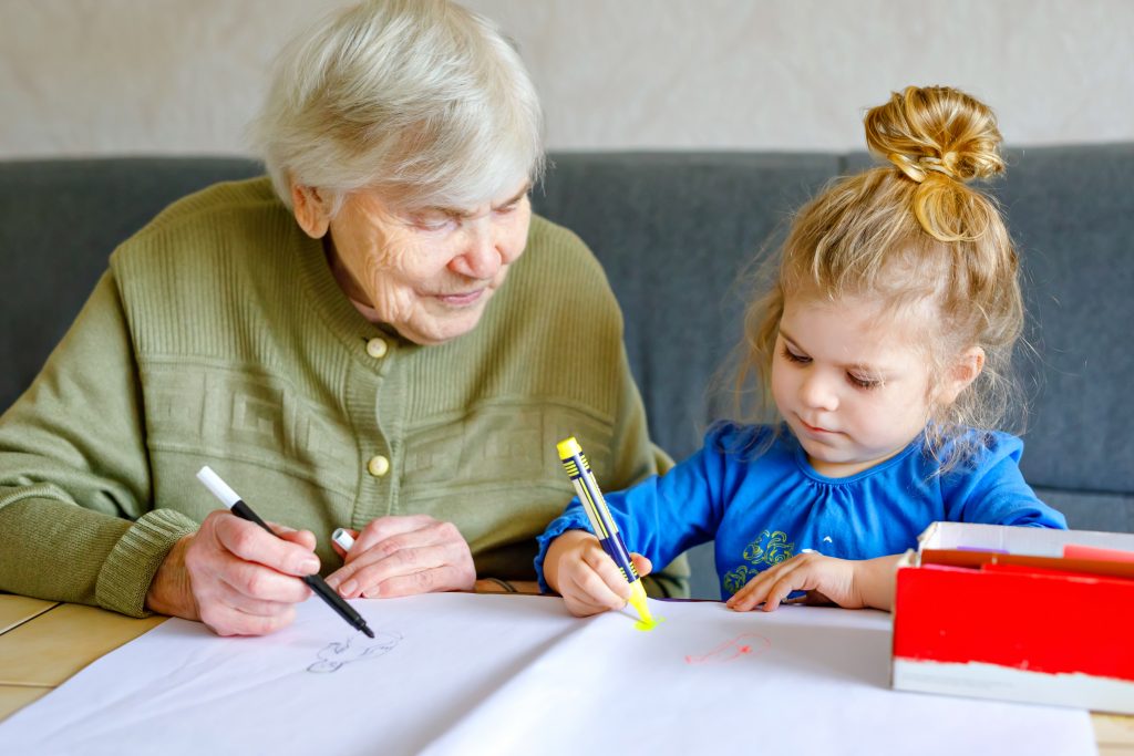 Elderly woman coloring with young girl.