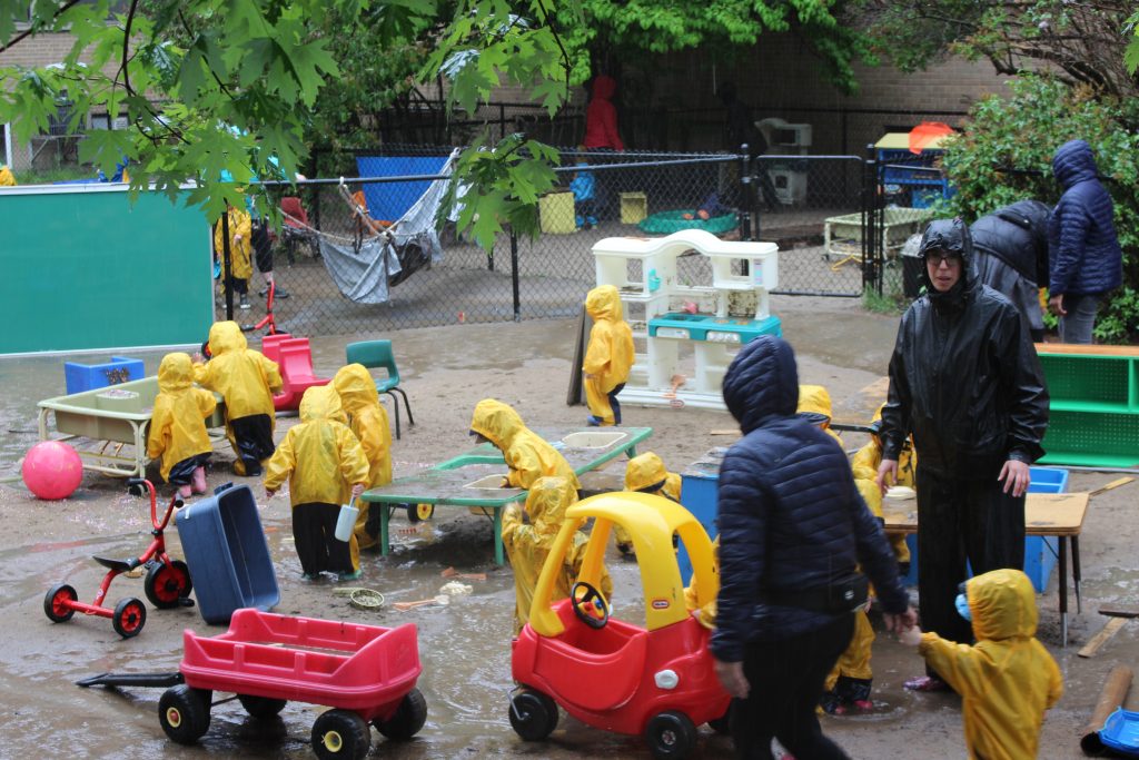 Many children playing outside with yellow raincoats.