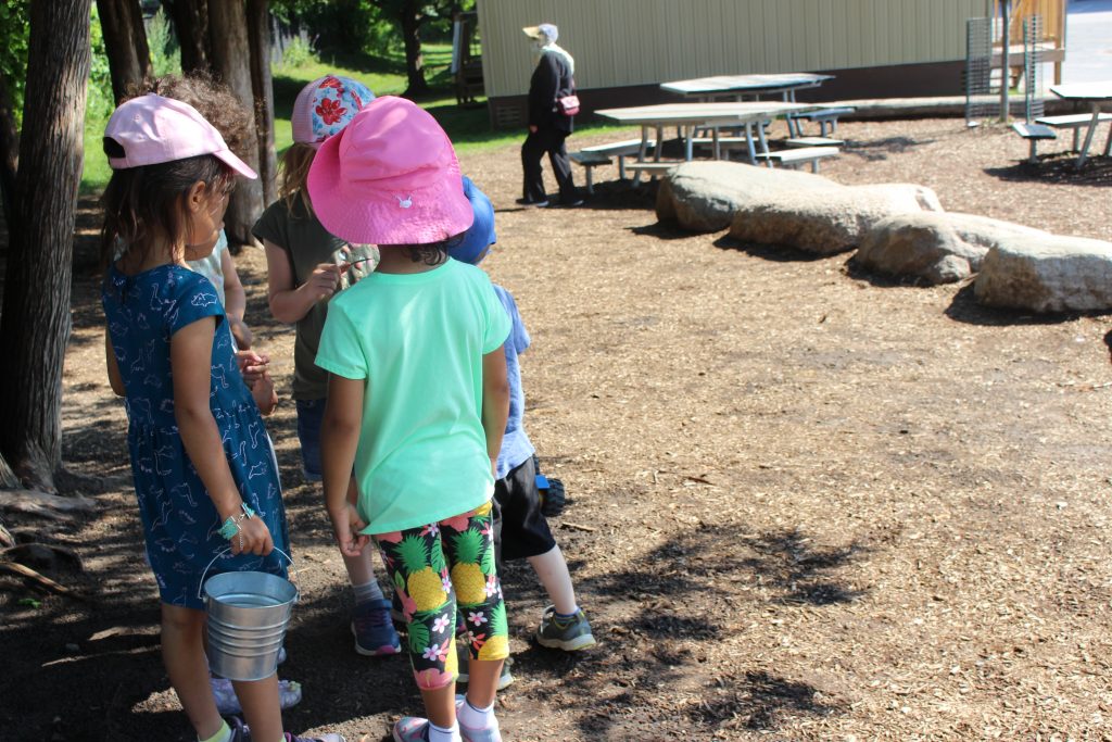 Children gathered to play with metal bucket outside.