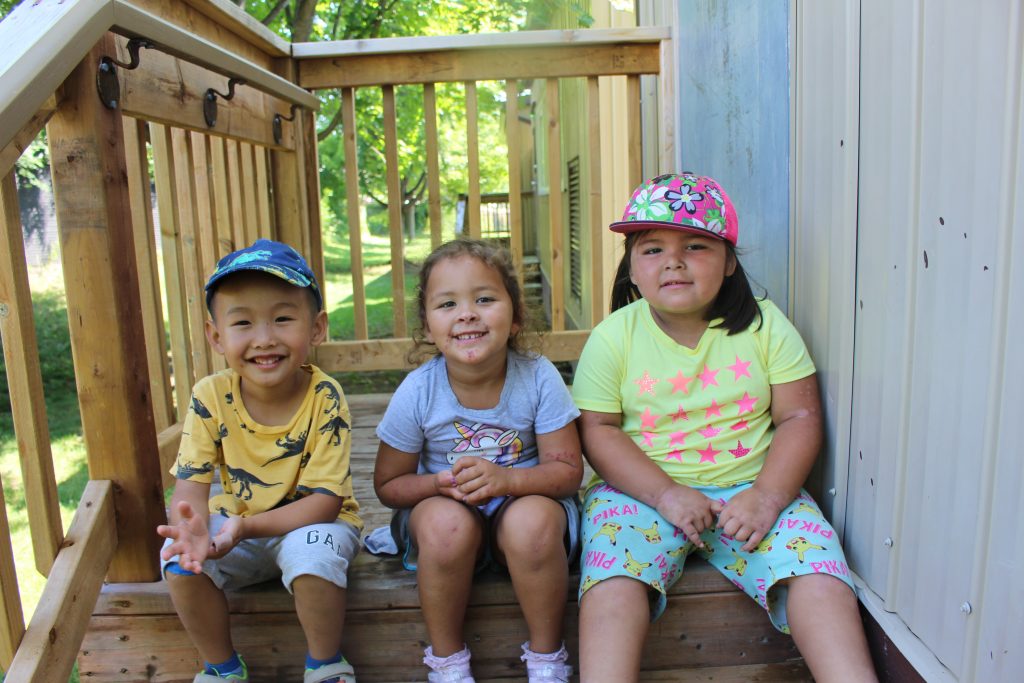 Enfants souriant assis sur un escalier en bois.