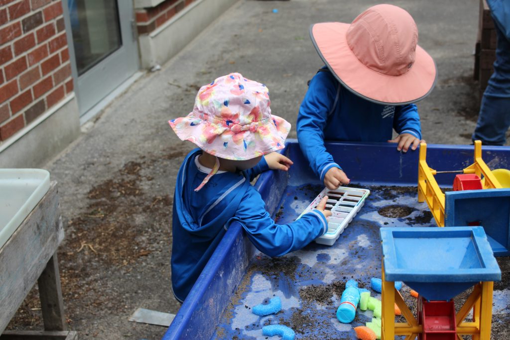 Children in pink hats playing outside with toys.