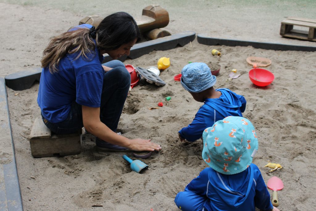 Female educator playing in sandbox with children.