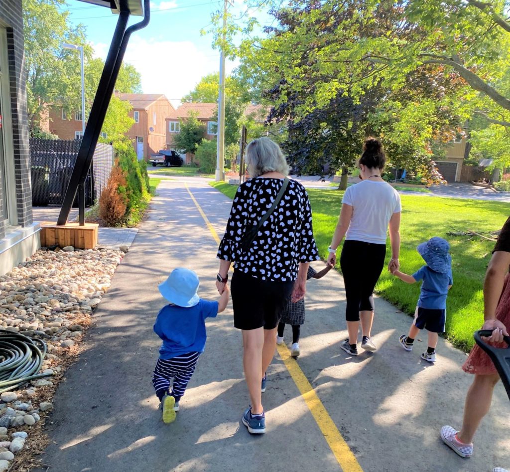 Older woman holding toddler's hand walking on road.