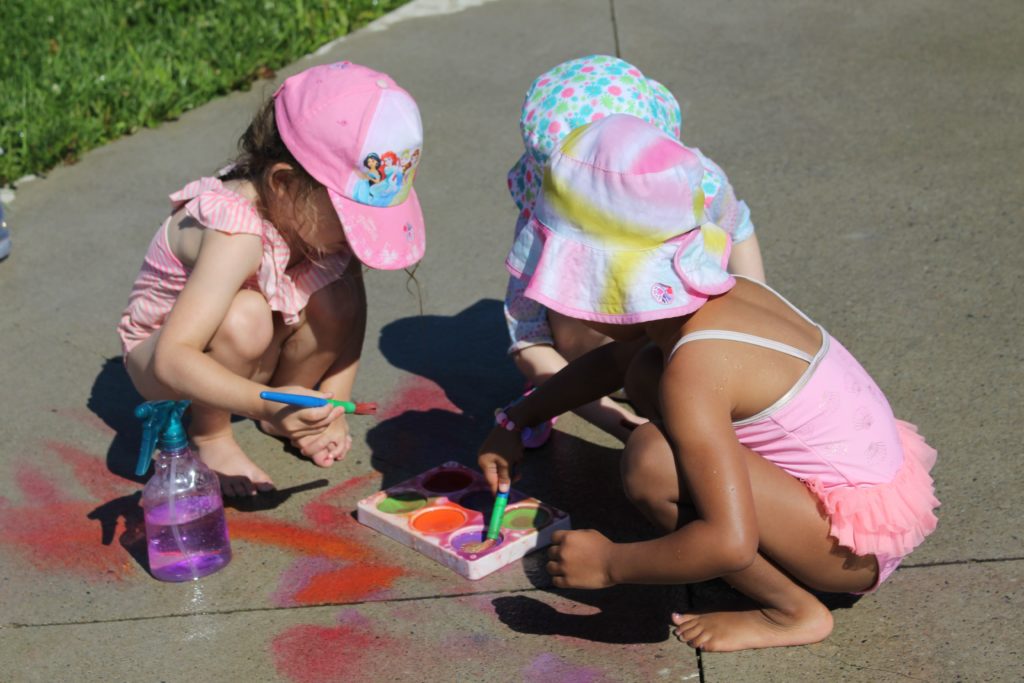 Three female toddlers painting on sidewalk.